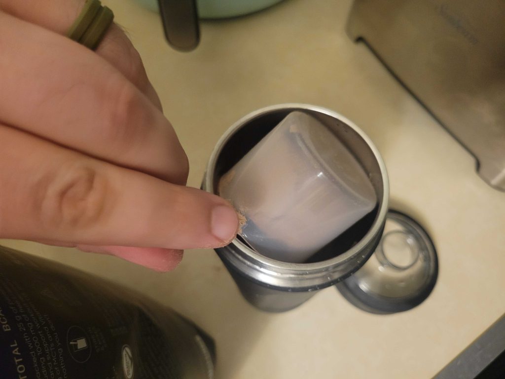 Someone dumping a scoop of Sports Research Whey Protein Isolate into a shaker bottle.