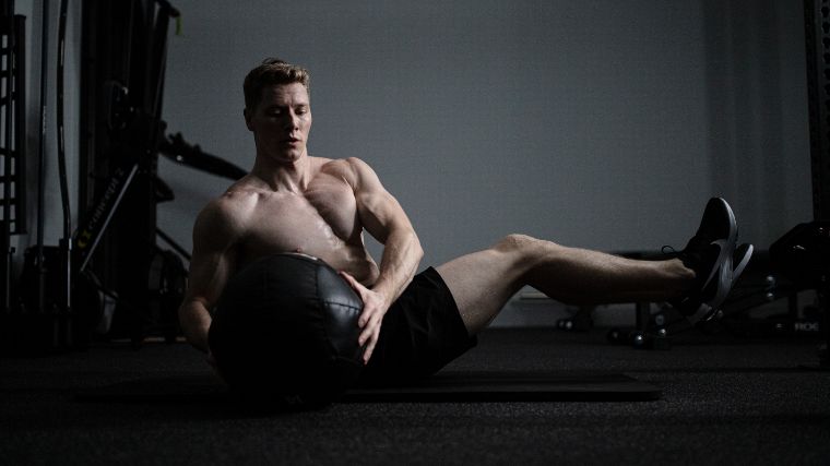 Josef Newgarden performing Russian twists with a medicine ball on the shirtless floor.