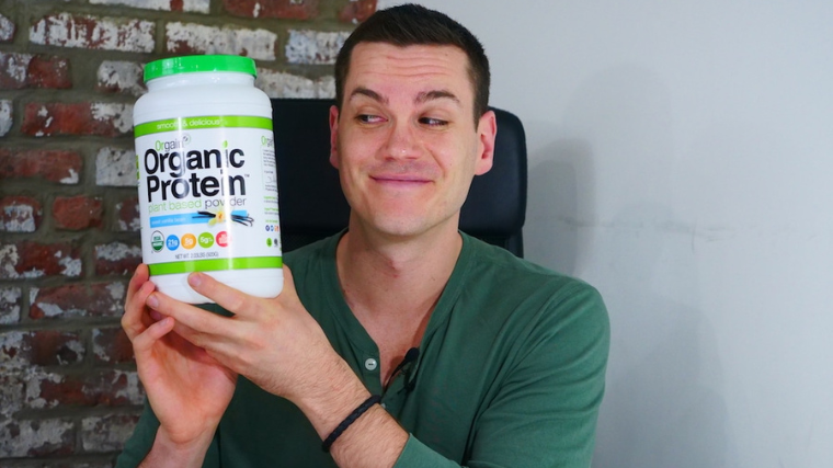 A person holds a tub of Orgain Organic Plant-Based Protein Powder.