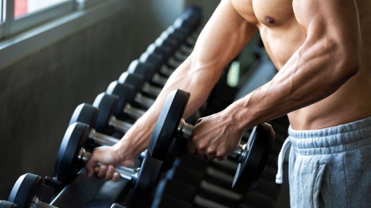 Shirtless man removes dumbbells from rack