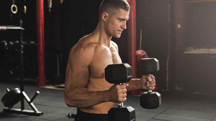A shirtless athlete performs hammer curls in the gym.