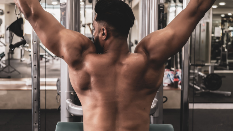 A shirtless athlete performs a lat pulldown.