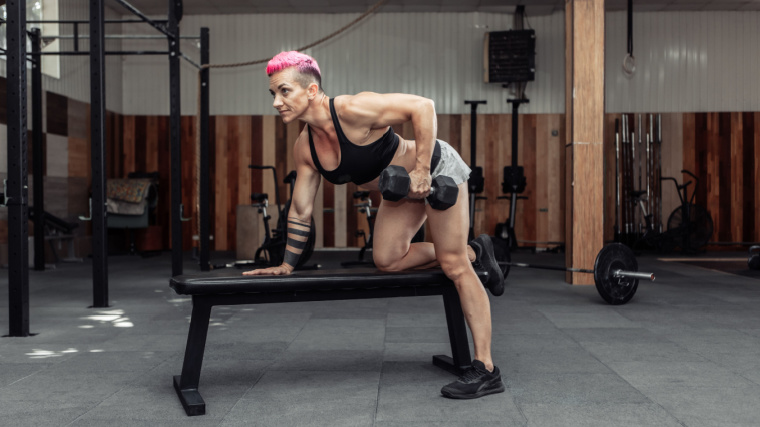 An athlete with pink dyed hair performs a single-arm dumbbell row.