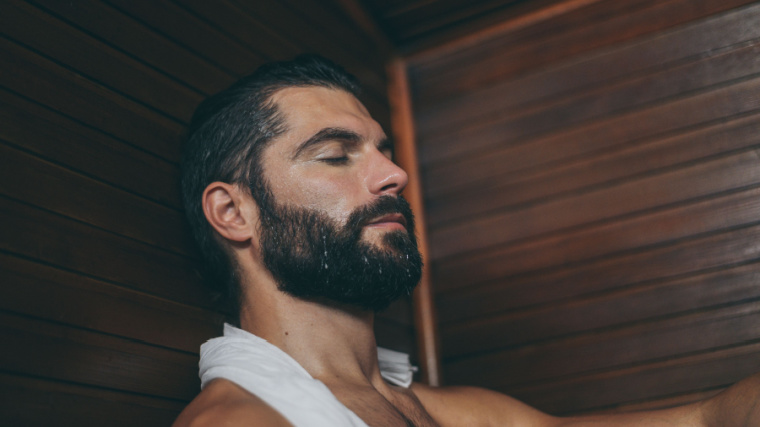 man with beard sweating in sauna with towel around his shoulders