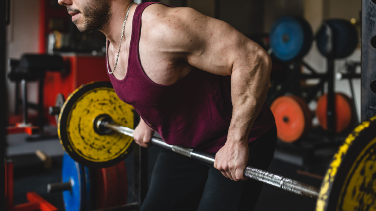 Man in red tank top focuses while performing bent-over row