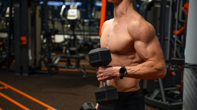 A shirtless athlete performs a hammer curl in the gym.