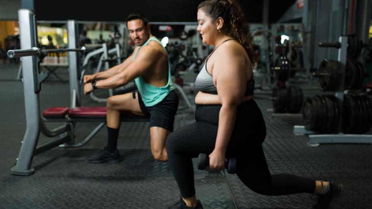 Two athletes perform lunges in the gym.