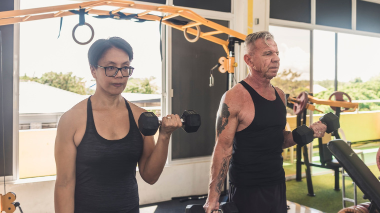 Two athletes perform biceps curls in a garage gym.