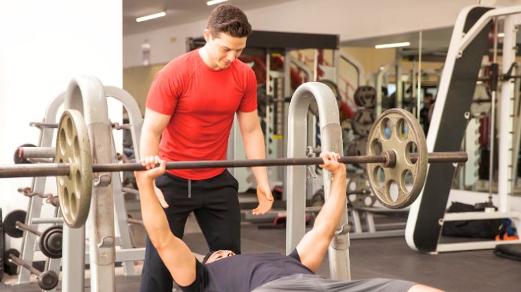 A spotter helping a gymgoer do eccentric bench presses.