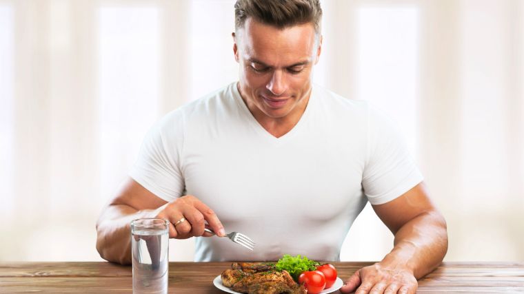 A bodybuilder getting ready to eat grilled chicken set on a plate.