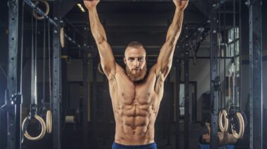 A muscular shirtless athlete doing pull-ups.