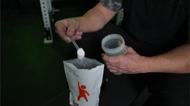 A person dumping a scoop of creatine into a shaker cup.