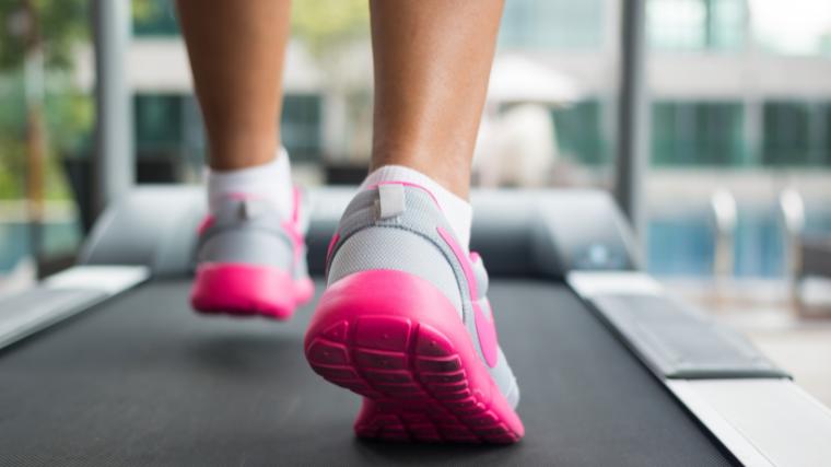 Feet in gray shoes with pink soles moving on a treadmill
