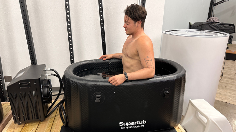 A shirtless person with top surgery scars sitting in the Hydragun Supertub.