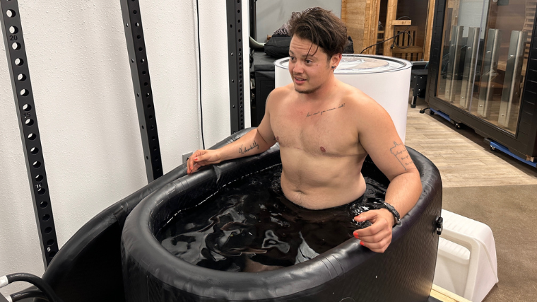 A shirtless person with top surgery scars sitting in the Hydragun Supertub.