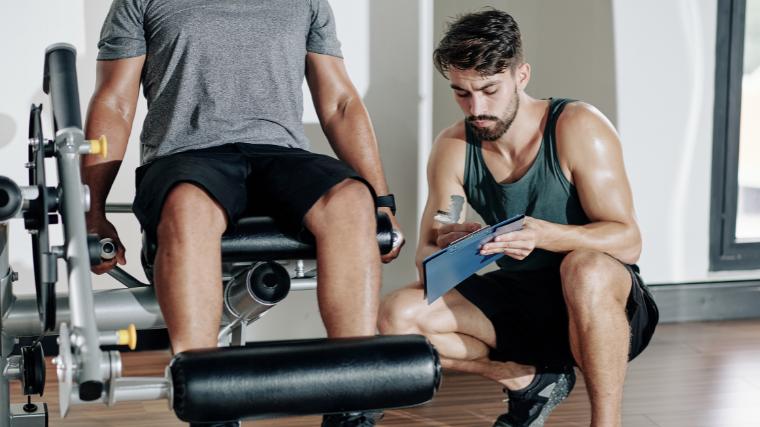 A person using the leg extension machine, with a coach checking his knees.