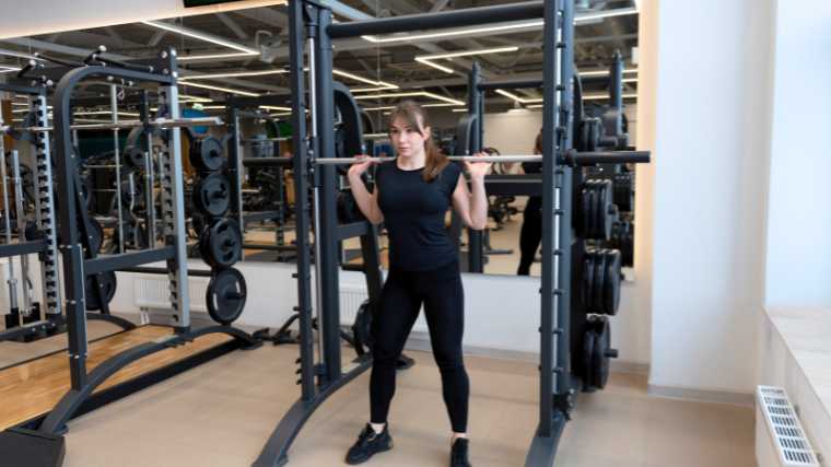 A person in black sportswear working out using a smith machine.