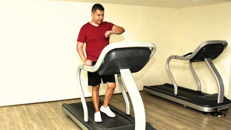 A person wearing a red shirt and black shorts walking on a treadmill.