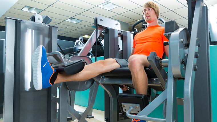 A person in an orange shirt doing unilateral exercises on the leg extension machine.
