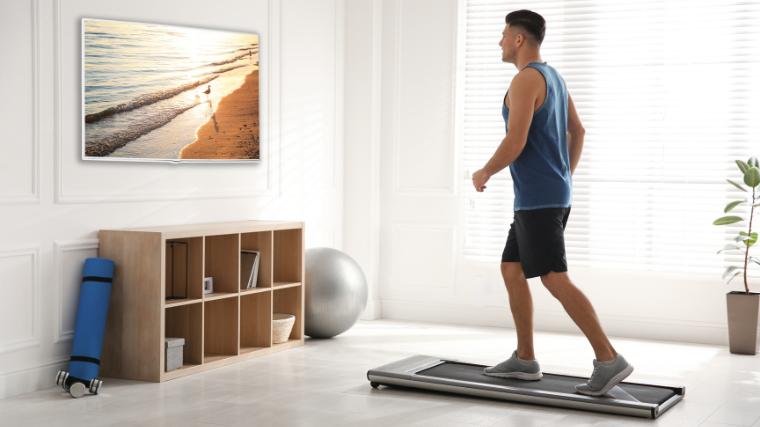 A person walking on a treadmill in front of a TV.