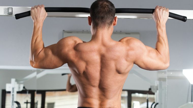 A muscular person doing a wide-grip pull up to work on his rear delts.