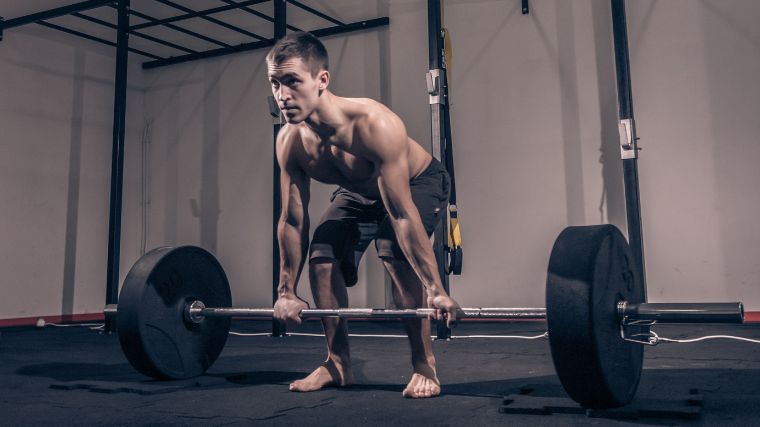 A muscular person deadlifting while barefoot.