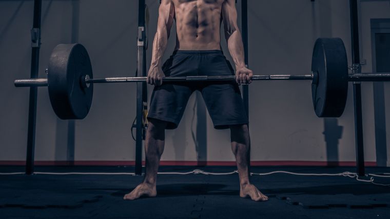 A shirtless person deadlifting a barbell while barefoot.