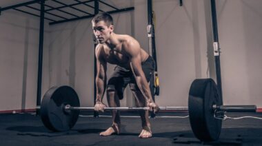 A muscular person deadlifting while barefoot.