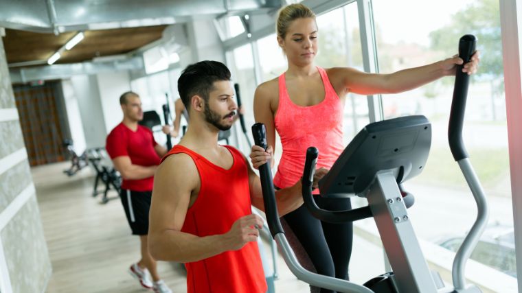 A gymgoer on the elliptical, and their personal trainer standing on the side.