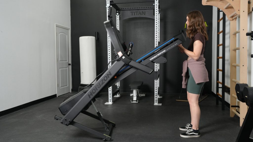 A woman is shown unfolding the Horizon 7.0 AT treadmill.