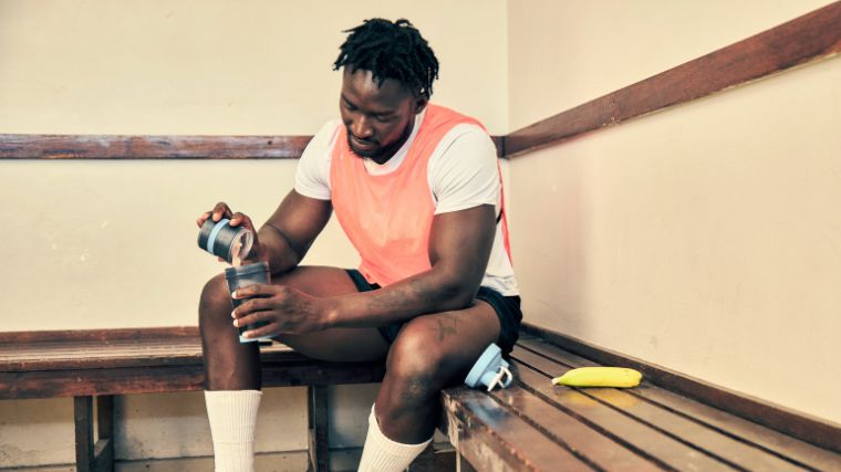 An athlete pouring protein powder in a shaker bottle.