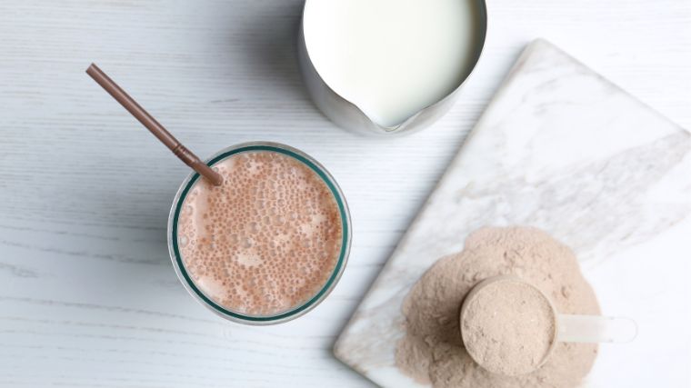 A glass of protein shake, a jug of milk and protein powder in a scoop.