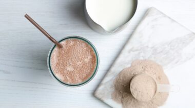 A glass of protein shake, a jug of milk and protein powder in a scoop.