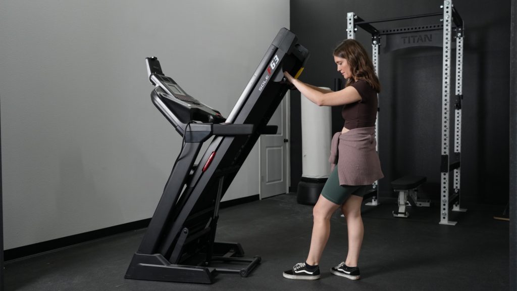 A woman folds up the Sole F63 treadmill.