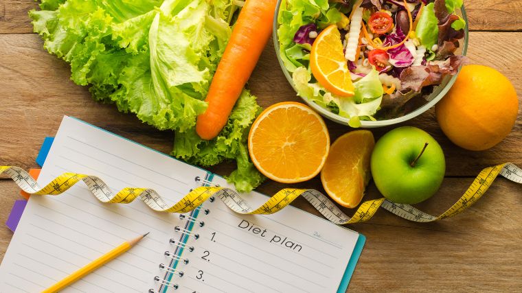 Fresh fruits and vegetables near a notebook with a diet plan.