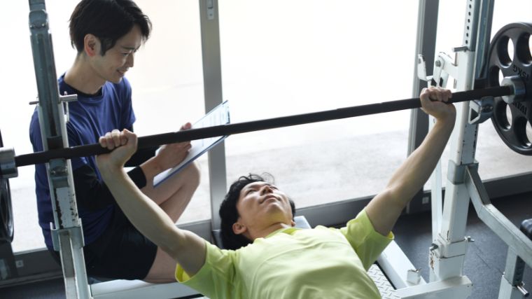 A person working out on the bench with a barbell with their coach.