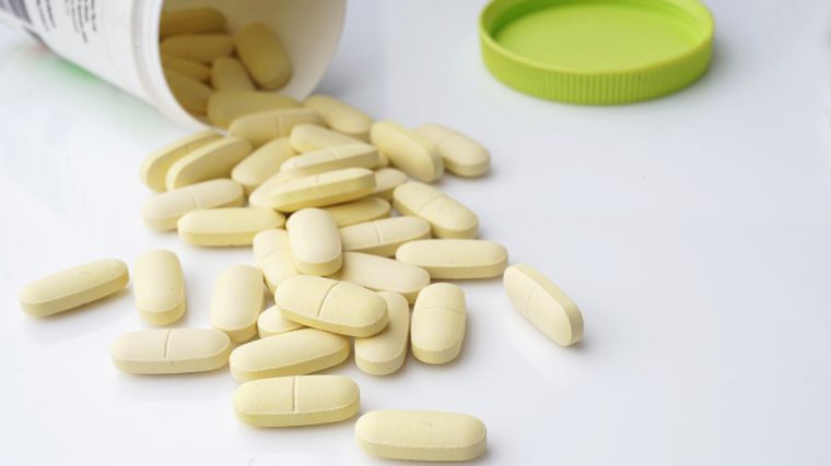 An open bottle of calcium supplements on it side with the tablets spilling out. 