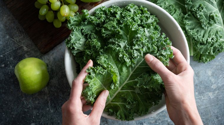 Kale being held by two hands over a white bowl. 
