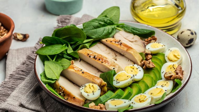 A plate with chicken, boiled eggs, avocado and spinach.