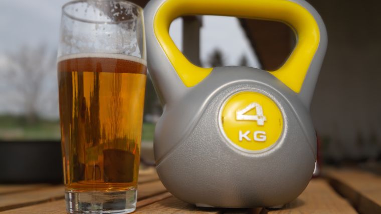 A glass of beer beside a yellow and gray kettlebell. 