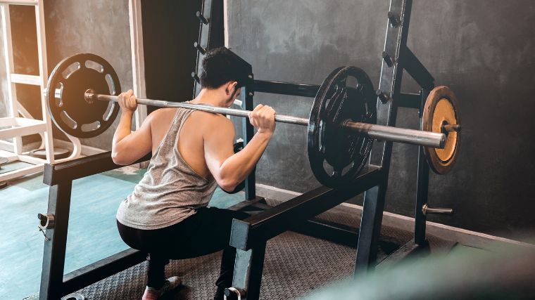 A gym goer squatting at a squat stand.