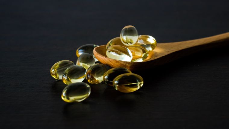 Vitamin D softgels om a wooden spoon and around the spoon. 