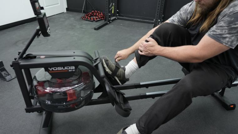 A man strapping his feet into the foot pedals of the Yosuda Water Rowing Machine