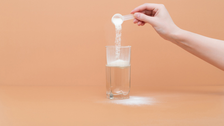 A person pouring a scoop of powder into a glass of water. 