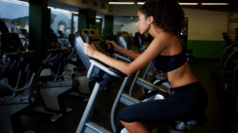 A person in black sports bra and leggings working out on a stationary bike in the gym.