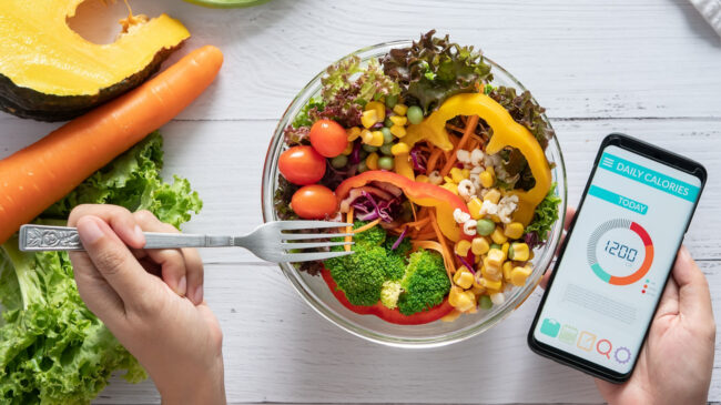 A bowl of healthy food and a smartphone with a calorie tracker app.