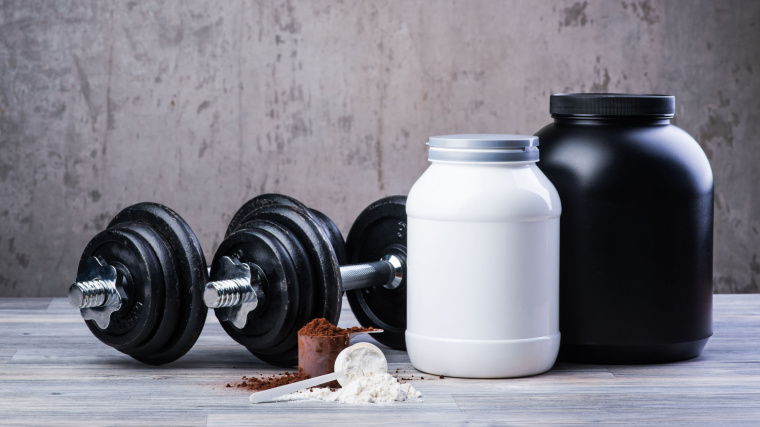 Mass gainer powder and whey powder in separate scoops beside their containers.