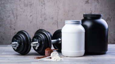 Mass gainer powder and whey powder in separate scoops beside their containers.