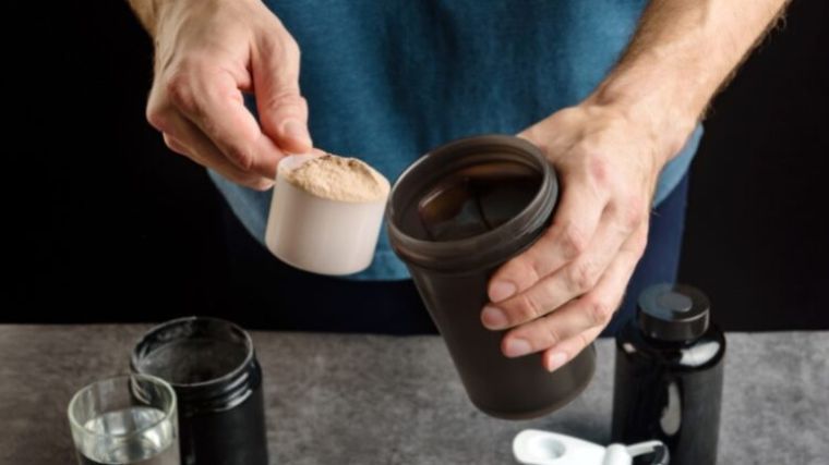 A person scooping protein powder into a shaker bottle.