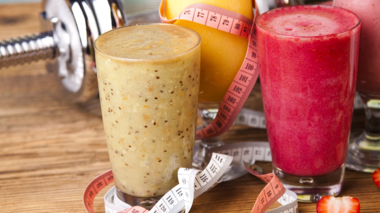 Two glasses of protein shake on a table with a measuring tape and dumbbell.